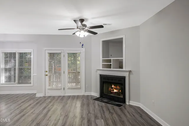 a view of an empty room with wooden floor fireplace and a window