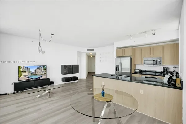a large white kitchen with granite countertop a stove a sink a refrigerator and white cabinets with wooden floor