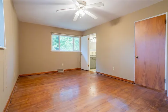 an empty room with wooden floor chandelier fan and windows
