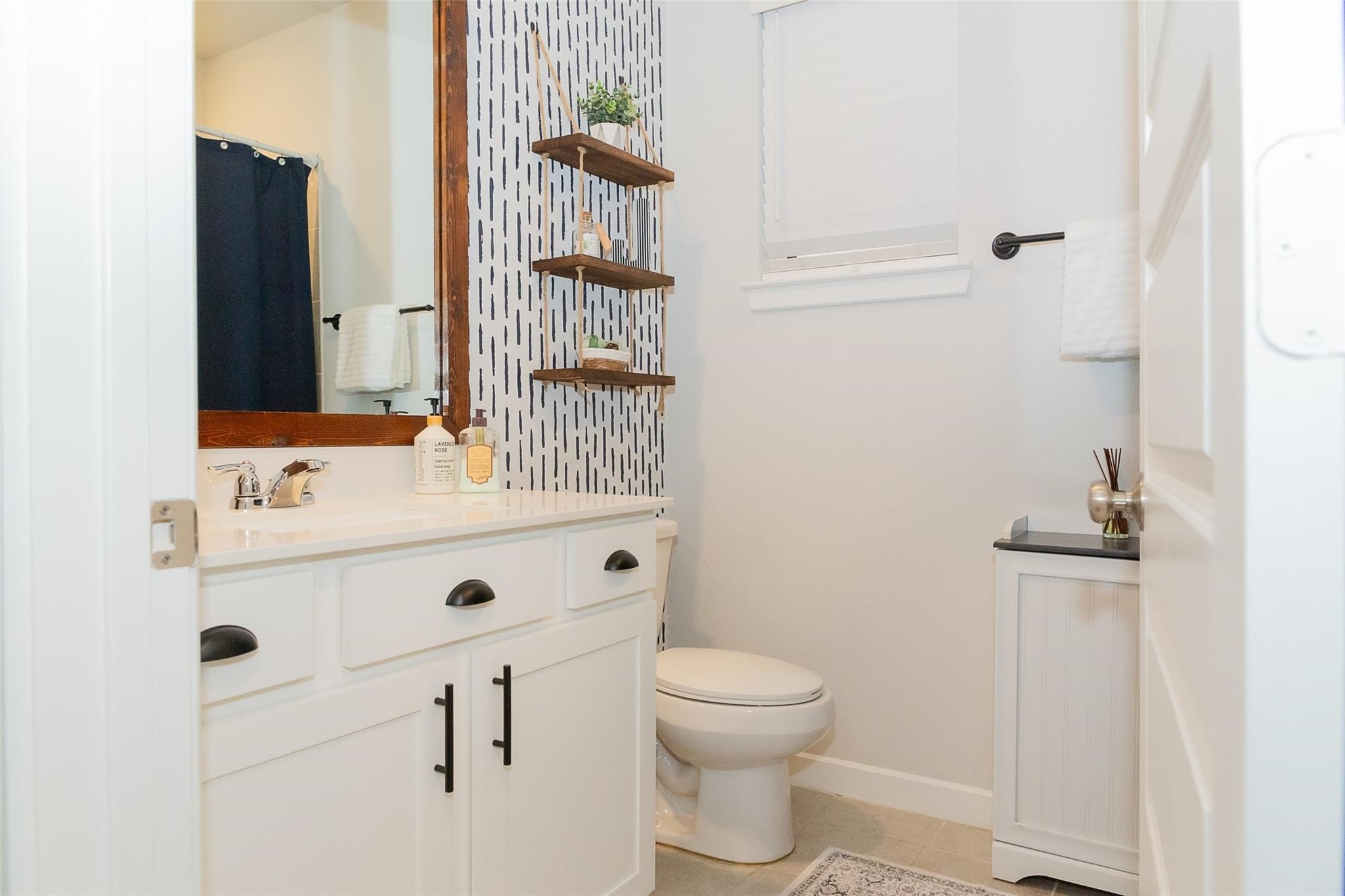 385 Weimer Lagoon Road La Porte, TX 77571 - Photo 17 of 22 This bathroom features a modern design with a white vanity, sleek black hardware, and a patterned accent wall, and a small window for natural light.