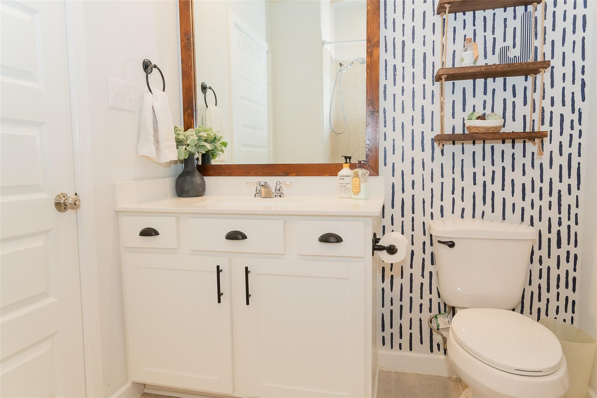 385 Weimer Lagoon Road La Porte, TX 77571 - Photo 18 of 22 This bathroom features a modern vanity with a large mirror, accented by a stylish patterned wallpaper.
