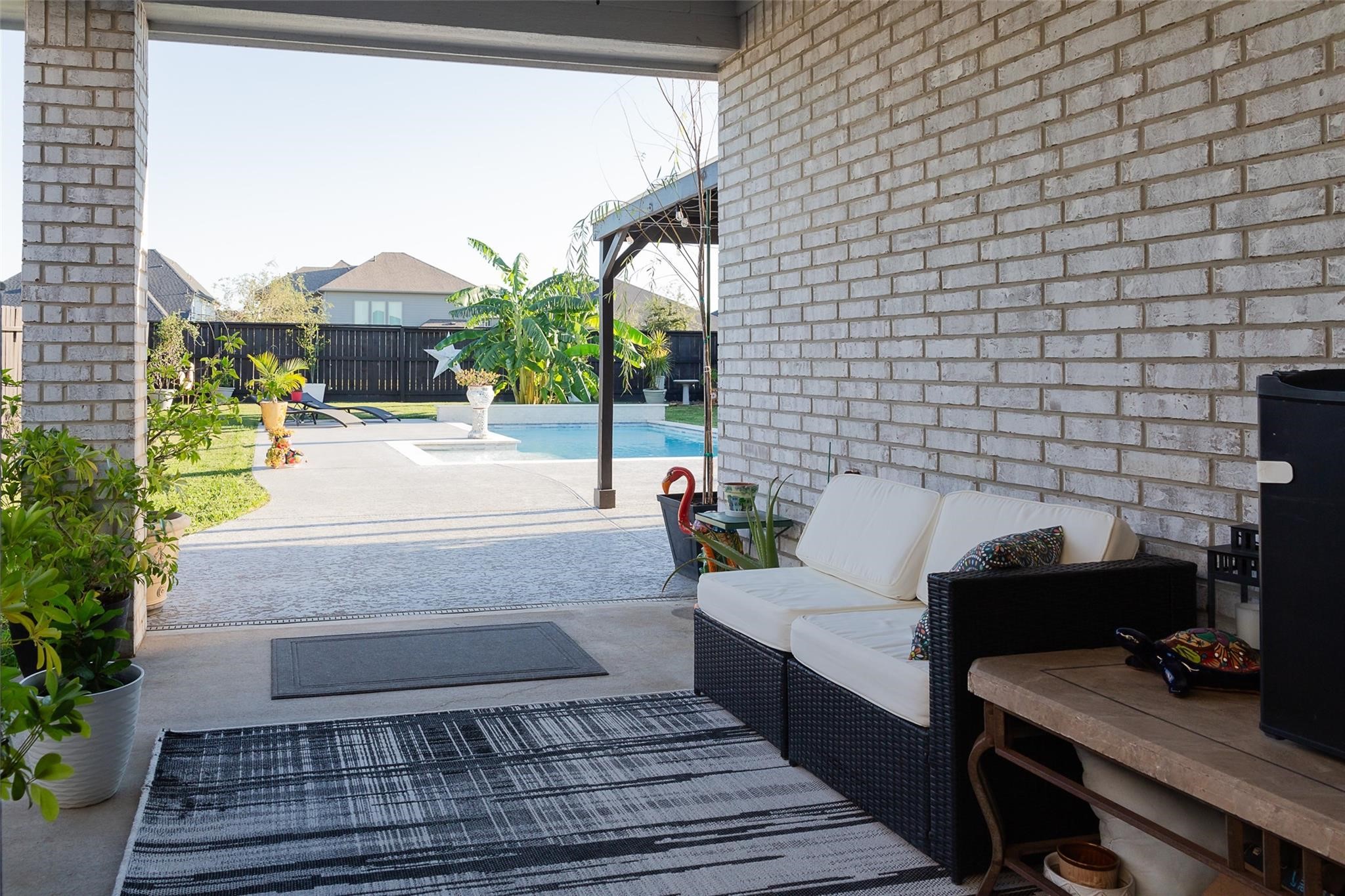 385 Weimer Lagoon Road La Porte, TX 77571 - Photo 19 of 22 This photo features a cozy covered patio area suitable for a comfortable seating arrangement, overlooking a well-maintained backyard with a swimming pool, offering a relaxing outdoor setting perfect for entertaining or lounging.