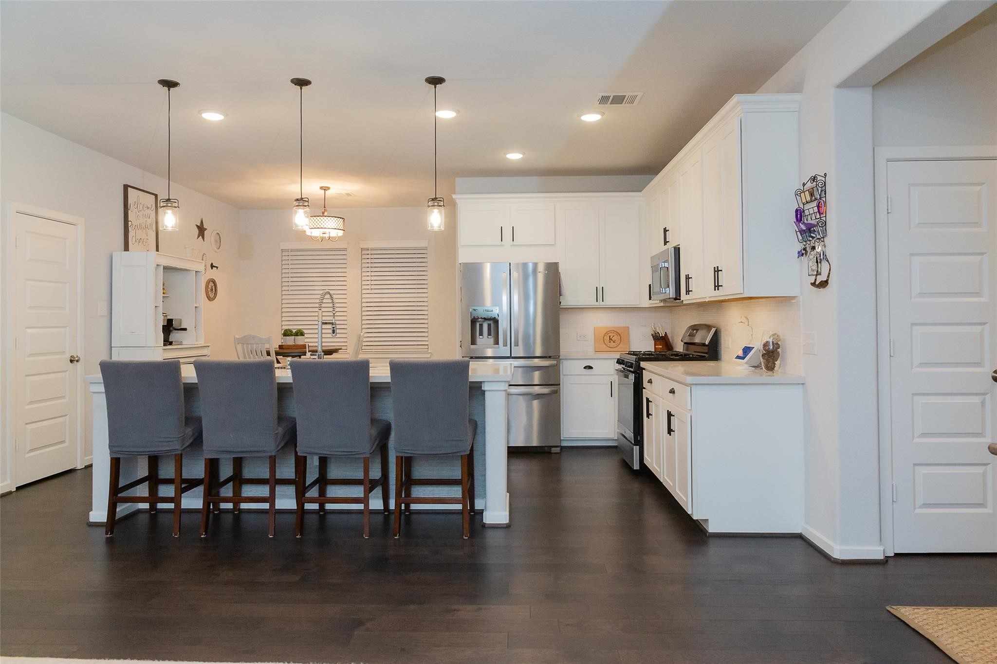 385 Weimer Lagoon Road La Porte, TX 77571 - Photo 4 of 22 This modern kitchen features sleek white cabinetry, stainless steel appliances, and a spacious island with seating for four. The open layout is complemented by stylish pendant lighting and dark hardwood floors, offering a warm and inviting space.