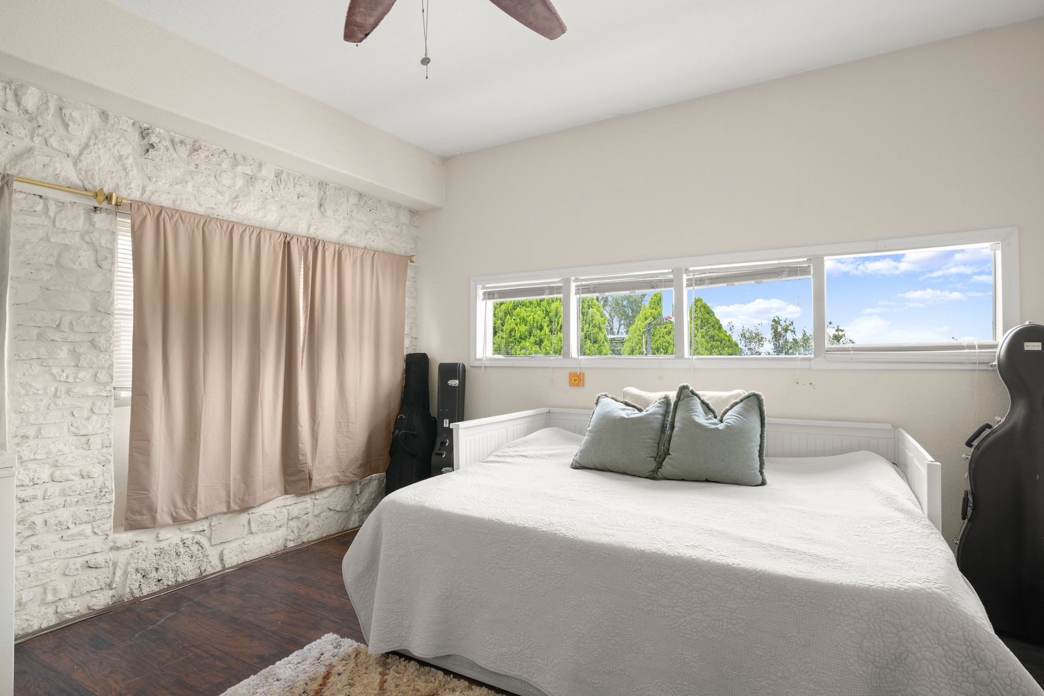 9725 Bock Road Buda, TX 78610 - Photo 17 of 32 A restful bedroom offers a wood-look floor, stone accent wall, and high windows providing natural light.
