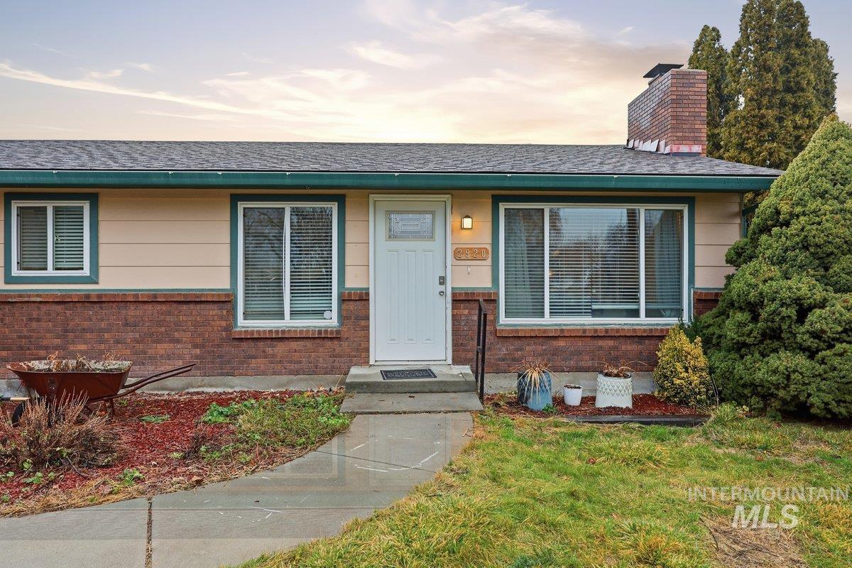 View of front of home with brick siding, a front lawn, a chimney, and roof with shingles