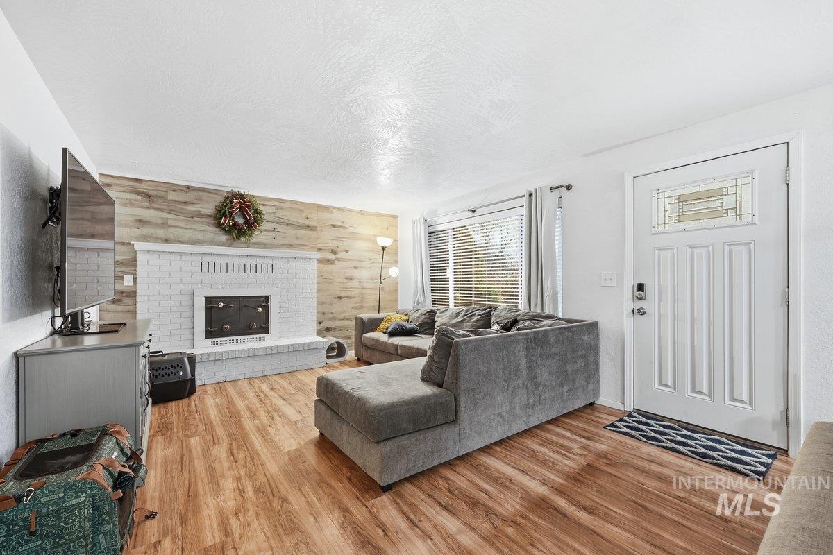 2920 South 10th Avenue Caldwell, ID 83605 - Photo 4 of 21 Living area featuring wooden walls, a textured ceiling, a brick fireplace, light wood finished floors, and an accent wall