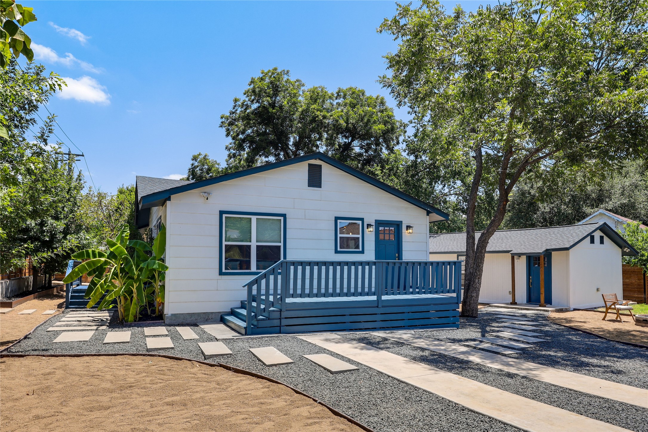 A charming cottage-style residence features a vibrant blue front door and porch, set against a crisp white exterior, surrounded by mature trees.
