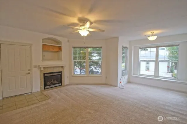 an empty room with windows fireplace and a ceiling fan