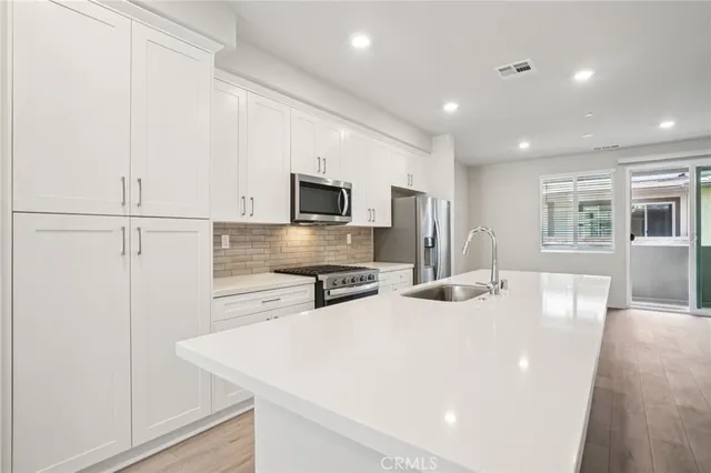 a kitchen with stainless steel appliances a white stove top oven a sink dishwasher and a refrigerator with wooden floor