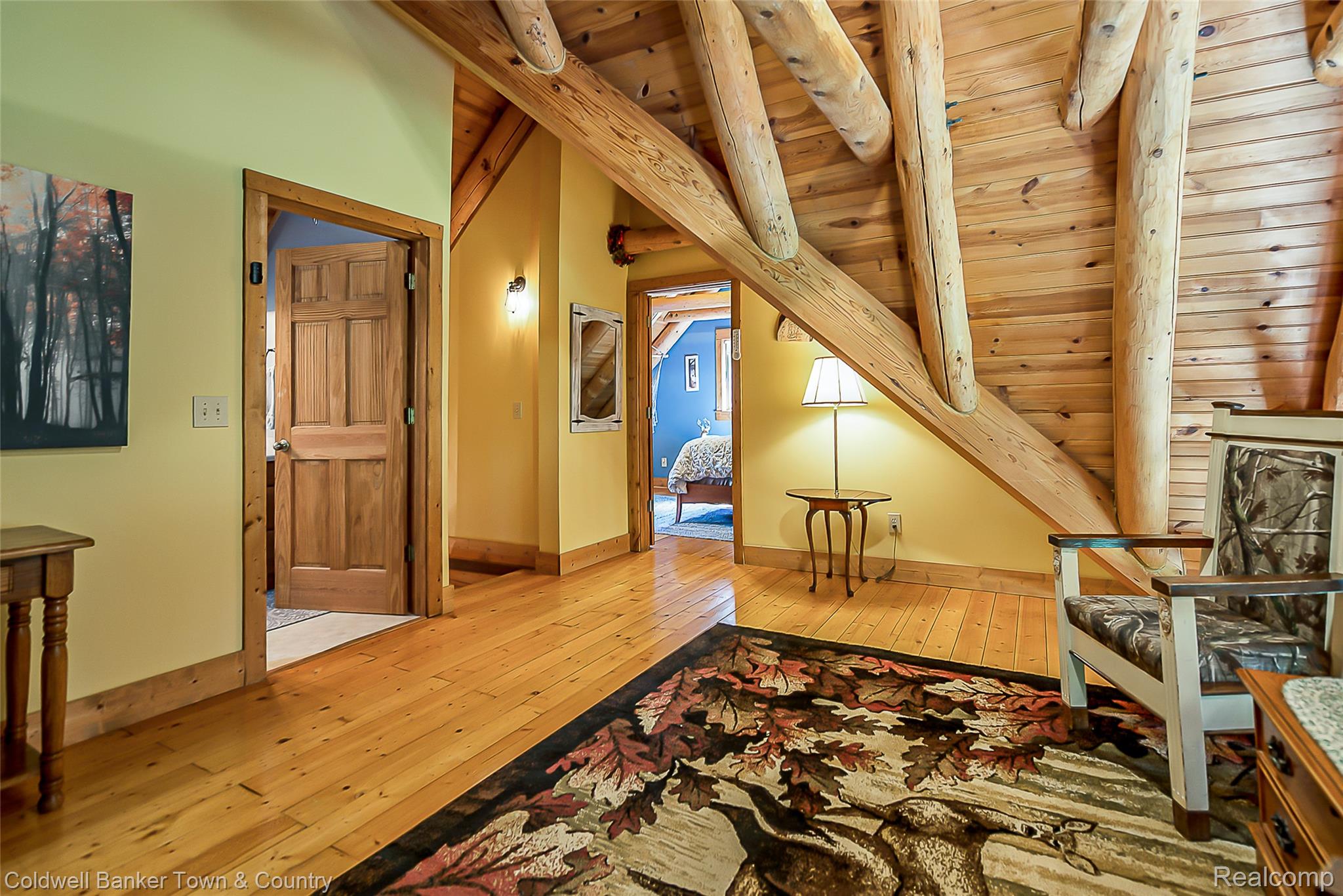 7023 Munsell Road Howell, MI 48843 - Photo 42 of 55 Wood-finish flooring, exposed log beam architecture, wood paneling, wood-frame doors, and wall sconce lighting