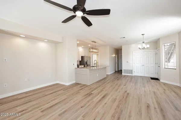 a view of an empty room and kitchen with wooden floor