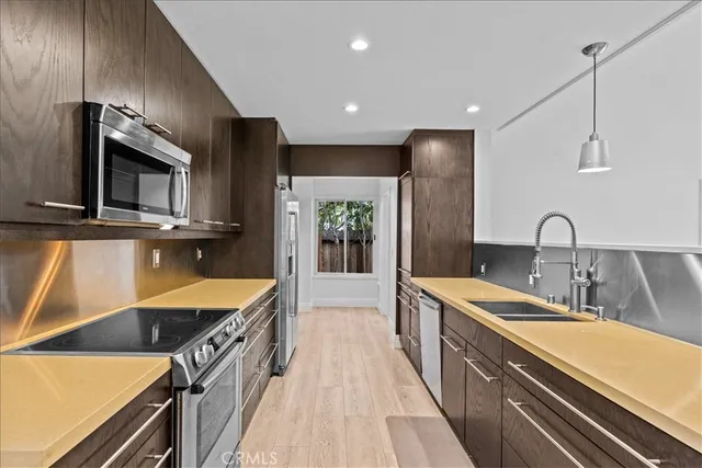 a kitchen with stainless steel appliances a sink dishwasher a stove top oven a refrigerator with wooden floor