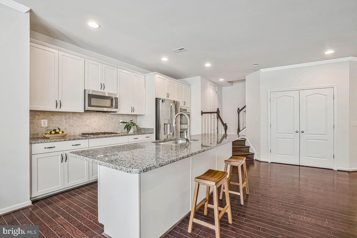 42523 Benfold Square Brambleton, VA 20148 - Photo 26 of 29 a kitchen with kitchen island granite countertop wooden floors white cabinets and appliances