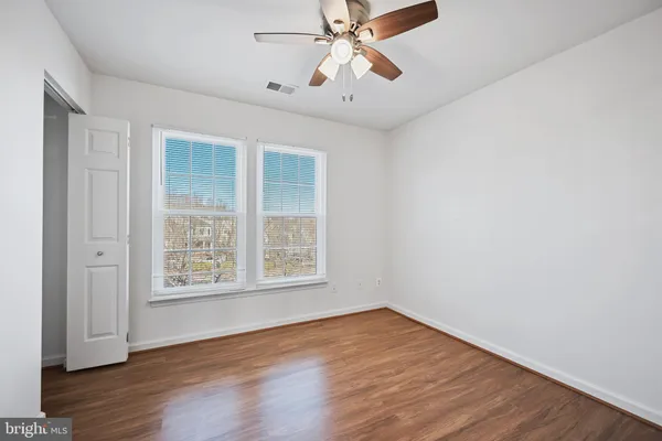 an empty room with wooden floor chandelier fan and windows
