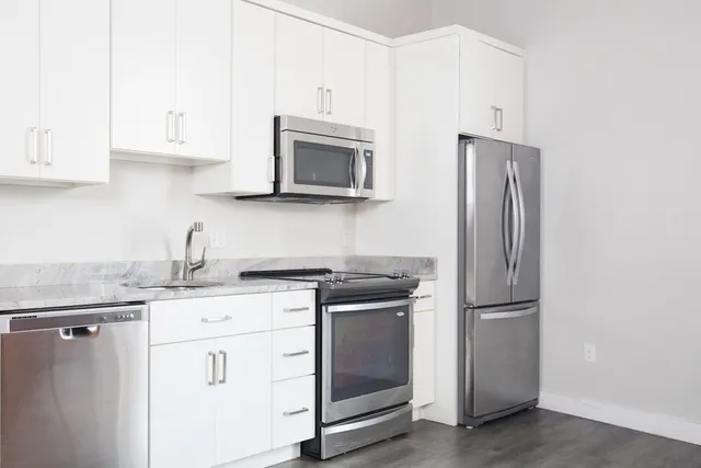 a kitchen with stainless steel appliances granite countertop white cabinets a refrigerator and a stove top oven