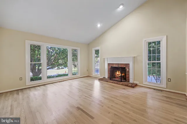 a view of an empty room with wooden floor fireplace and a window
