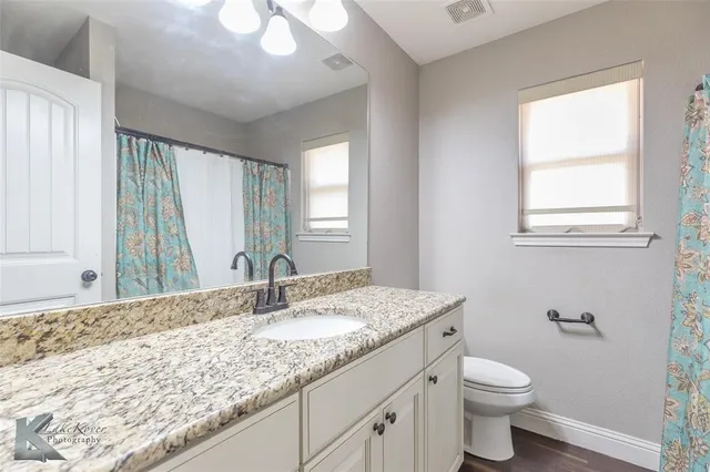 a bathroom with a granite countertop sink toilet and large mirror