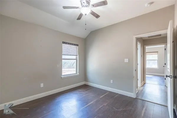 an empty room with wooden floor fan and windows