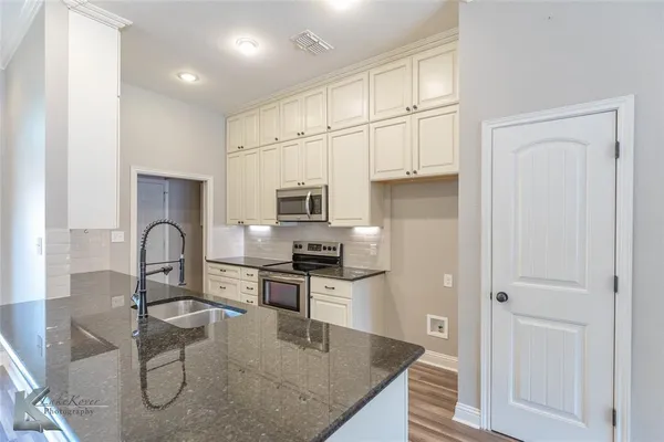a kitchen with stainless steel appliances granite countertop a stove top oven a sink dishwasher and white cabinets with wooden floor