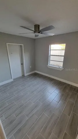 an empty room with wooden floor fan and windows