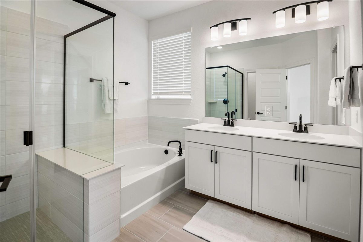 104 Raleigh Drive Georgetown, TX 78633 - Photo 22 of 37 A well-appointed bathroom offers a glass-enclosed shower, a relaxing soaking tub, and a dual vanity with a wide mirror.