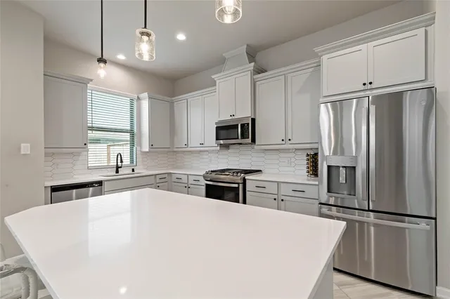 a white kitchen with granite countertop a refrigerator oven a sink dishwasher and white cabinets with wooden floor