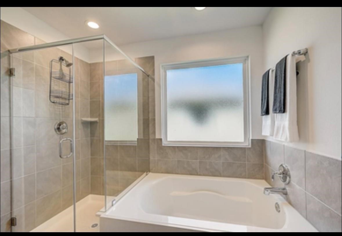 1246 Truckee River Drive Rosharon, TX 77583 - Photo 15 of 23 Modern bathroom featuring a glass-enclosed shower, a spacious bathtub, and large frosted window for natural light. Neutral tile accents complement the sleek fixtures.