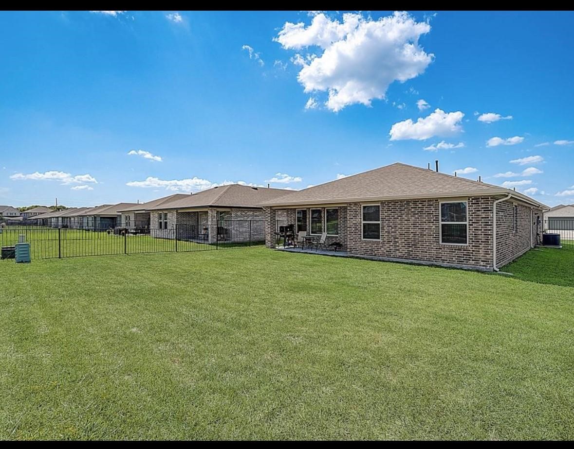 1246 Truckee River Drive Rosharon, TX 77583 - Photo 22 of 23 Spacious backyard with well-maintained lawn, bordered by a brick house featuring multiple windows and a patio area. Ideal for outdoor activities and relaxation.