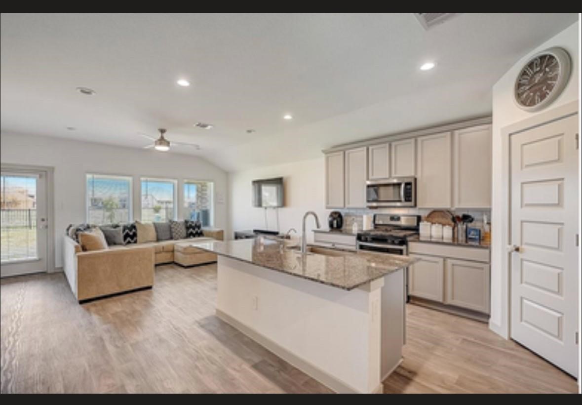 1246 Truckee River Drive Rosharon, TX 77583 - Photo 5 of 23 This photo showcases a spacious open-concept living area with a modern kitchen featuring stainless steel appliances and a large island. The room is well-lit with natural light from multiple windows, and a comfortable seating area is adjacent to the kitchen. The space is perfect for entertaining and family gatherings.