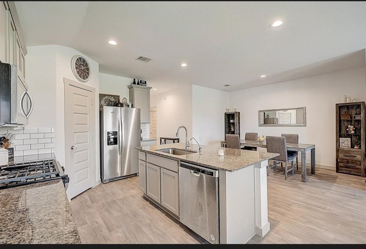 1246 Truckee River Drive Rosharon, TX 77583 - Photo 6 of 23 Modern kitchen with granite countertops, stainless steel appliances, and a central island with a sink. The space flows into a dining area with a stylish table and ample seating, offering an open-concept feel.
