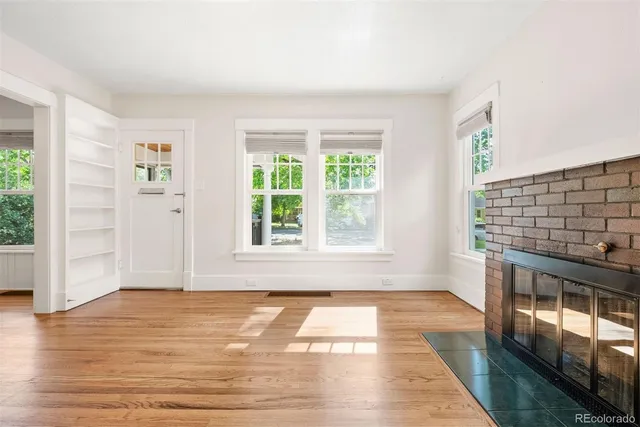 a view of an empty room with wooden floor fireplace and a window