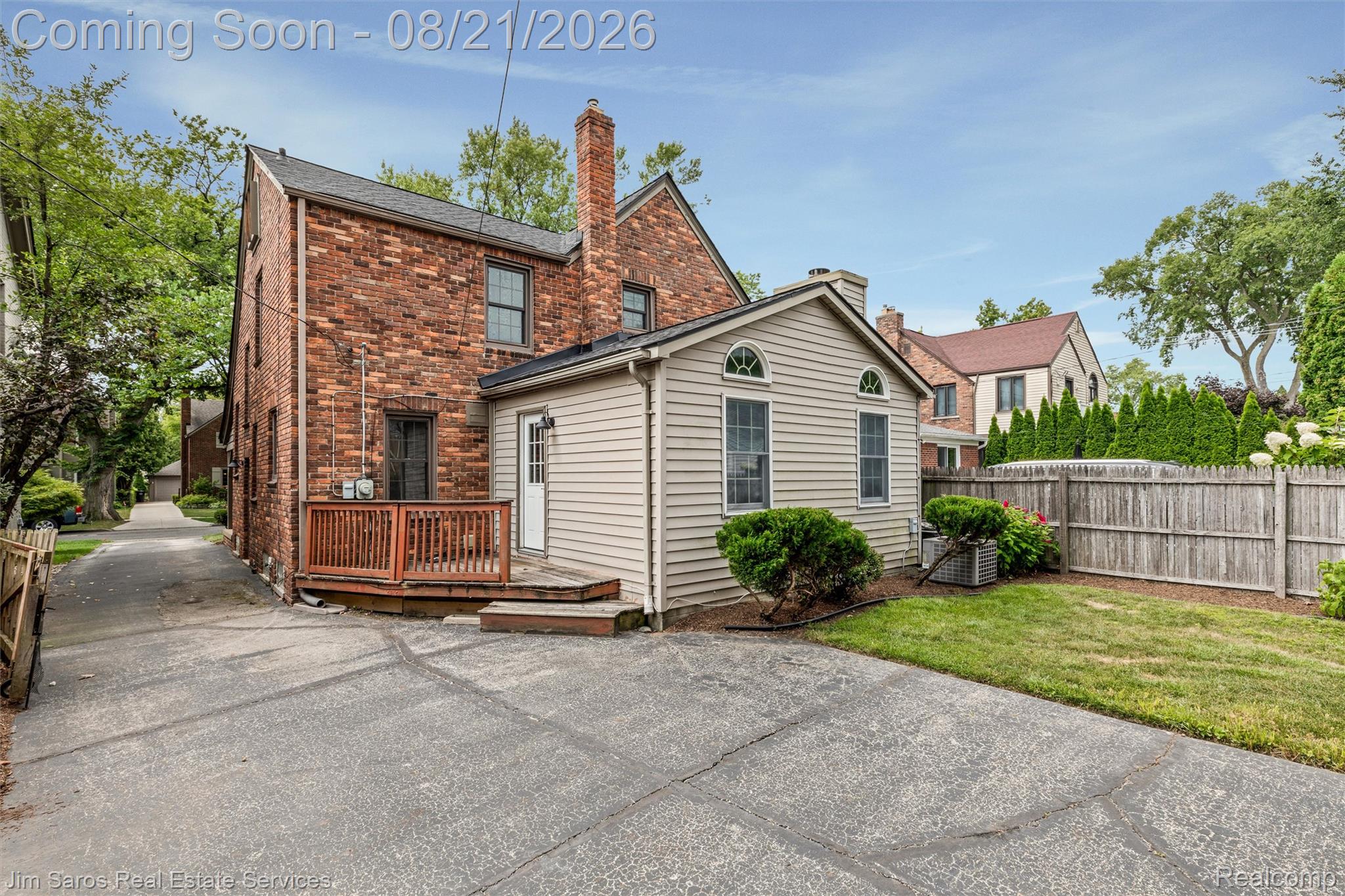 288 Moran Road Grosse Pointe, MI 48236 - Photo 21 of 24 Brick exterior with an attached siding addition, featuring a raised wood deck, paved driveway, and a wooden privacy fence enclosing a grassy area