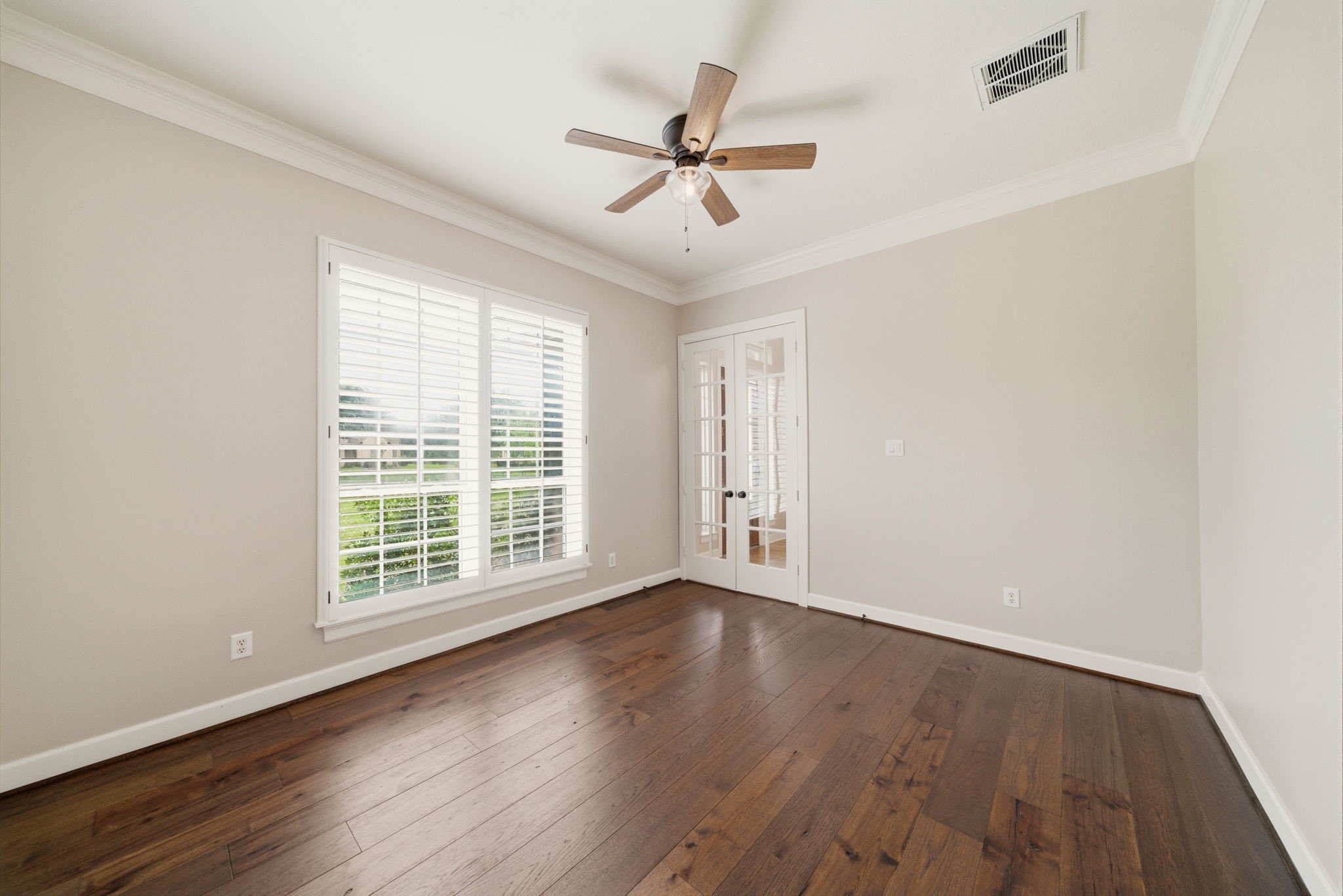4535 Box Turtle Lane Fulshear, TX 77441 - Photo 12 of 49 This room features elegant hardwood floors, a ceiling fan, and ample natural light from large windows with white shutters. French doors add a touch of sophistication, making it perfect for a home office or cozy retreat.
