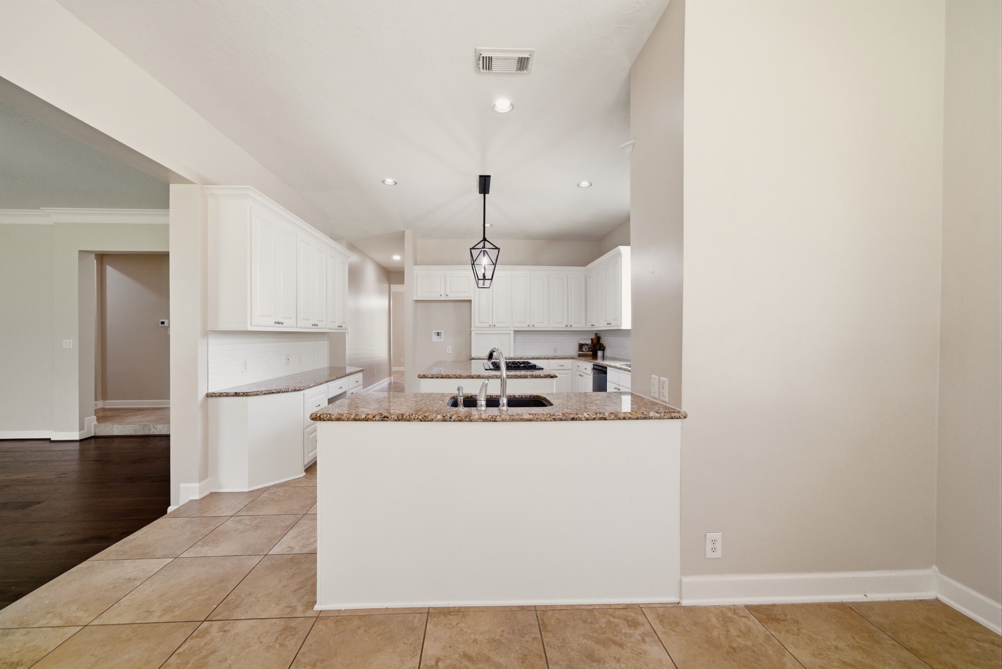 4535 Box Turtle Lane Fulshear, TX 77441 - Photo 19 of 49 This kitchen features a spacious layout with white cabinetry, granite countertops, and a central island with a sink. It opens to an adjacent living area with tile flooring, creating a seamless flow for entertaining.