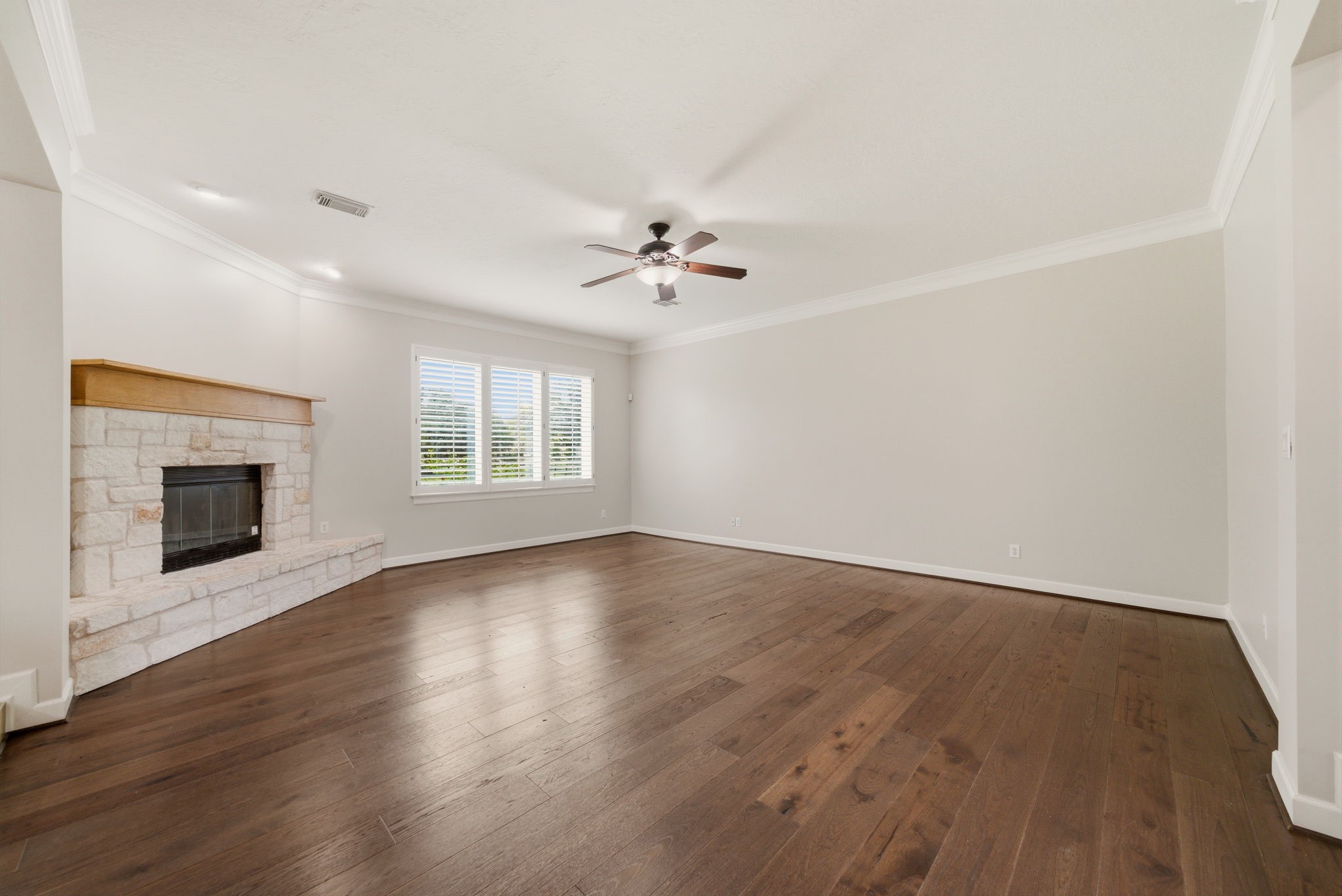 4535 Box Turtle Lane Fulshear, TX 77441 - Photo 21 of 49 This spacious living room features hardwood floors, a stone fireplace, and a ceiling fan. Large windows with shutters provide plenty of natural light.