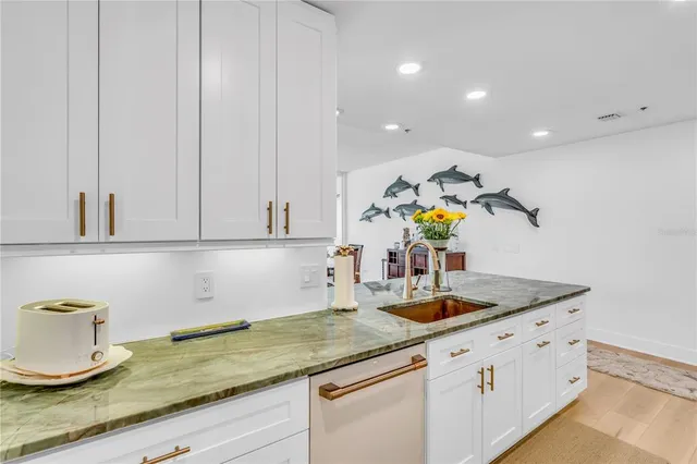 a kitchen with stainless steel appliances granite countertop a sink a stove and white cabinets with wooden floor