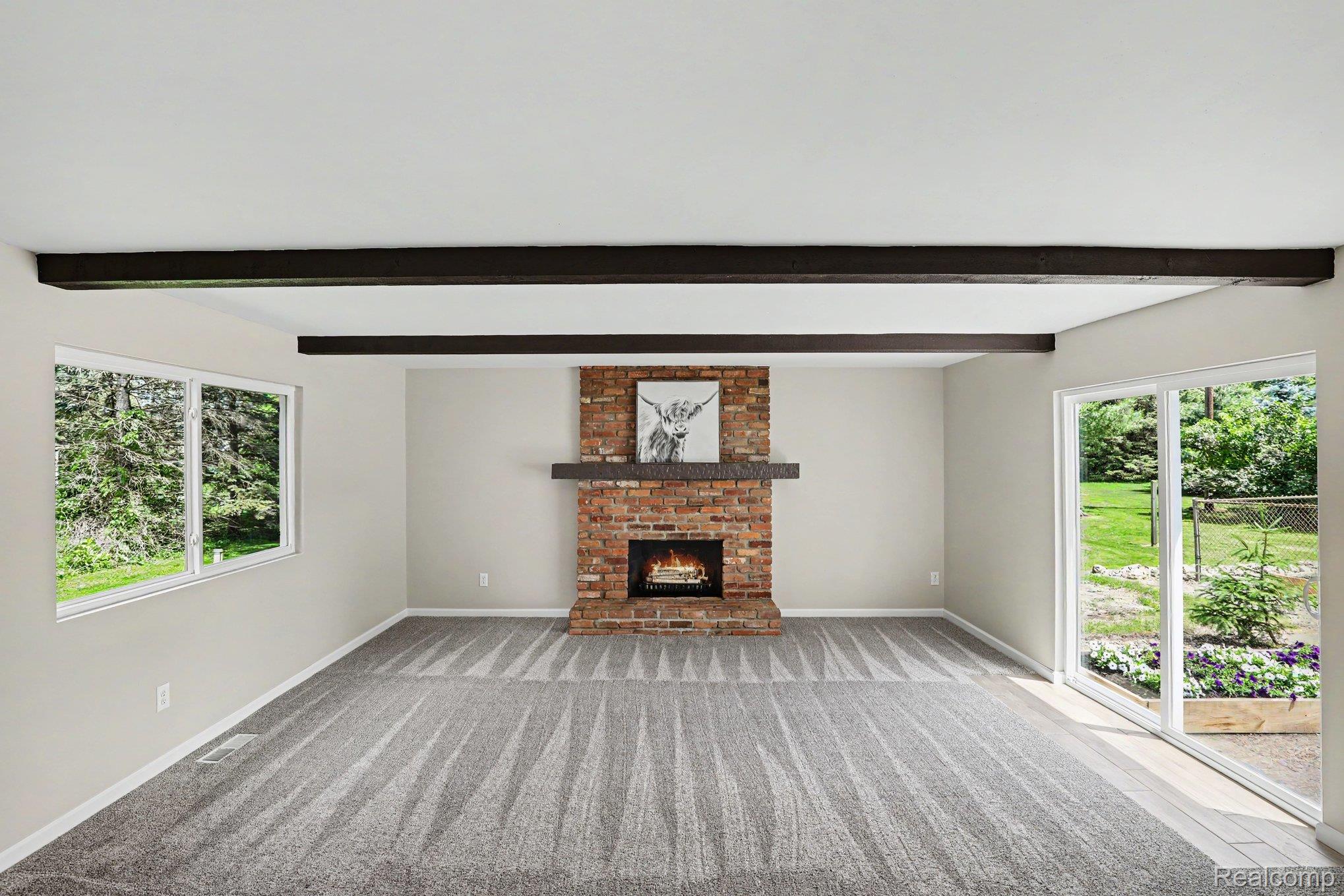 74600 Nordman Court Romeo, MI 48065 - Photo 3 of 32 Living area featuring a brick fireplace with a wood mantel, exposed ceiling beams, and patterned carpeting