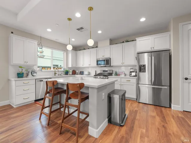 a kitchen with stainless steel appliances a refrigerator a stove a sink dishwasher and a dining table with wooden floor