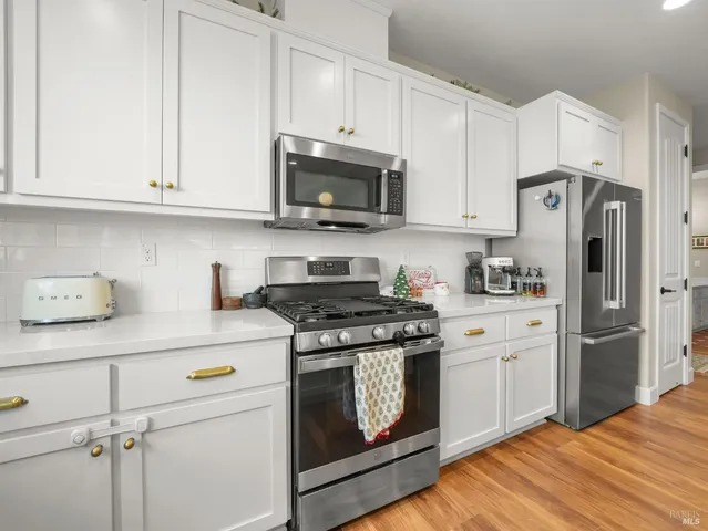 a kitchen with stainless steel appliances white cabinets and a stove a refrigerator with wooden floors