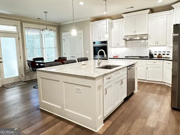 a kitchen with a stove a sink a refrigerator and white cabinets with wooden floor