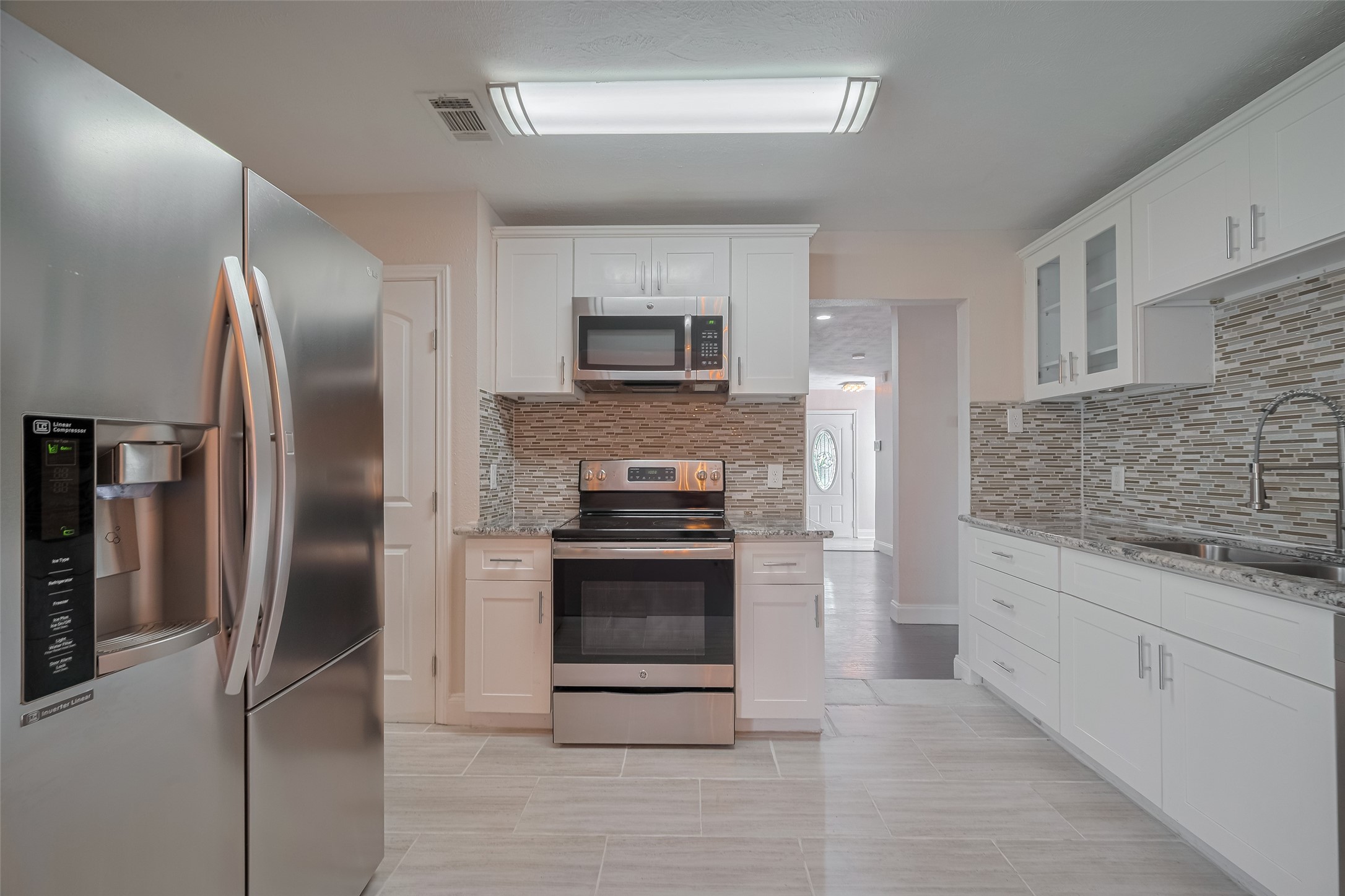 3930 Daphne Street Houston, TX 77021 - Photo 16 of 44 Clean lines define this efficient kitchen—crisp white cabinetry, gleaming countertops, and a lovely backsplash play beautifully under contemporary linear lighting. Just off to the side: a dedicated laundry zone.