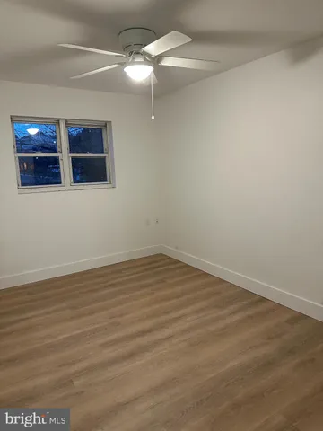 a view of an empty room with wooden floor and a ceiling fan