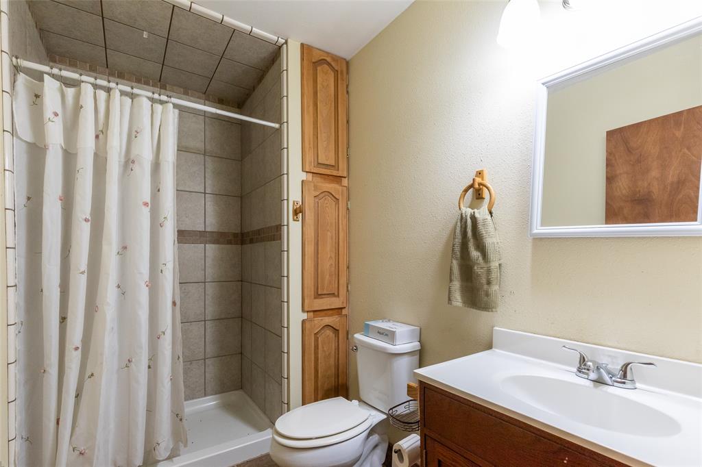 640 Ground Street Moran, TX 76464 - Photo 14 of 35 Full bathroom featuring a tiled shower with a decorative accent band, a single vanity with a white countertop and integrated sink, a large wall-mounted mirror, and wood-finish cabinetry