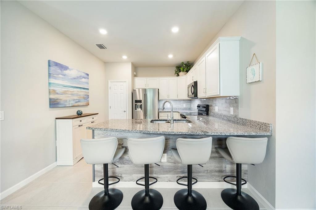 6125 Triumph Lane Ave Maria, FL 34142 - Photo 9 of 31 Kitchen featuring white cabinetry, a kitchen breakfast bar, stainless steel fridge with ice dispenser, decorative backsplash, and light stone countertops