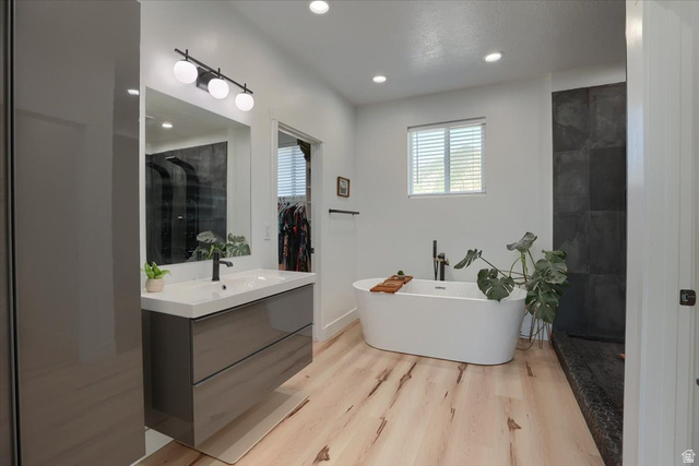 828 South Deer Road Tooele, UT 84074 - Photo 48 of 51 Bright bathroom featuring a floating vanity with integrated sink, contemporary black fixtures, light wood-finish flooring, a freestanding soaking tub, and large format dark tile in the shower