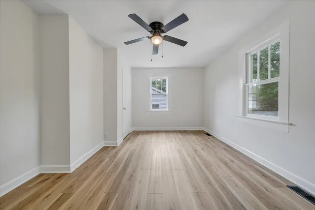 an empty room with wooden floor chandelier fan and windows
