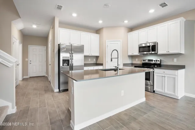 a large kitchen with stainless steel appliances granite countertop a stove a sink a refrigerator and white cabinets with wooden floor