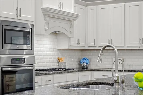 a kitchen with stainless steel appliances granite countertop a refrigerator a sink dishwasher a stove and white cabinets with wooden floor