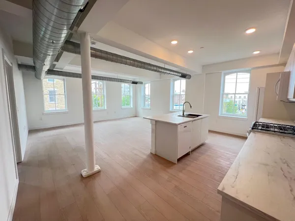 a large kitchen with kitchen island granite countertop a stove a sink a refrigerator and white cabinets with wooden floor