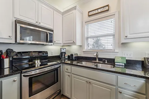 a kitchen with granite countertop white cabinets appliances and a window